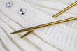 White knitted garment with gold colored knitting needles