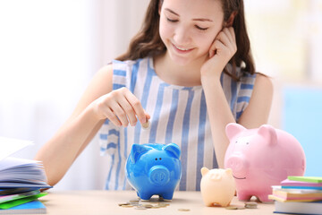 Poster - Young smiling girl putting coins into piggy bank on light background. Saving for education concept