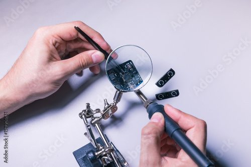 Plakat Inżynier montuje PCB (płytka drukowana), lutując mikrochip za pomocą pincety i szkła powiększającego