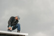 © Daniil - A man in work clothes tighten screws with a screwdriver on the roof against a cloudy sky.