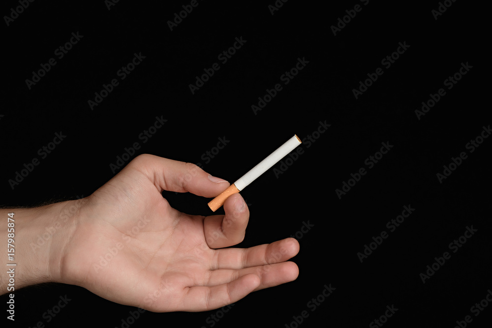 holding cigarette between middle and ring finger Man's hand holding a cigarette between index finger and thumb in the shape  ring. isolated on black background Stock Photo