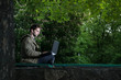 © Олександр Болюх - Young handsome student sitting on a wooden bench in the park with laptop computer.