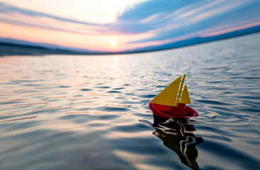 Wall Mural - A small children's yellow red boat sails on the sea against the background of the sunrise