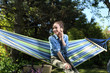 Mój piękny ogród.Młoda atrakcyjna kobieta wypoczywa na hamaku w ogrodzie rozmawiając przez telefon