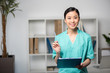 © LIGHTFIELD STUDIOS - smiling asian internist holding pen and clipboard with diagnosis in professional clinic