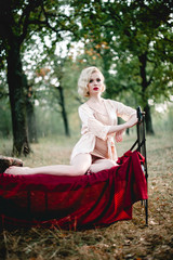 Beautiful and elegant blonde woman with red lips and hair waves wearing beige nightie posing on the bed outdoors autumn, retro vintage style and fashion. fine art toning shot