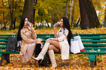 charming brunette girlfriends drinking coffee sitting on bench in the park