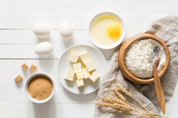 Wall Mural - Baking bread or baking cake ingredients. 
Cubed butter, brown sugar, eggs and white flour on white wooden table. Rustic style baking / cooking ingredients. Top view