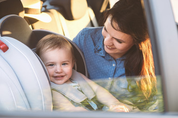 Mother securing her toddler girl buckled into her baby car seat