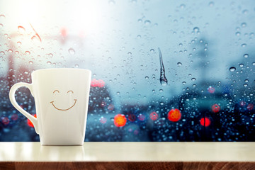 happy coffee mug with smilely face on desk inside glass window, blurred traffic jam light in city as