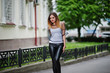 Fashionable woman look at white shirt, black transparent clothes, leather pants, posing at street against iron fence. Concept of fashion girl.