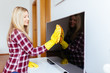© hedgehog94 - Beautiful young smiling woman cleaning TV with microfiber cloth.