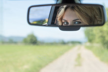 The beautiful eyes of the young driver woman are reflected in the rearview mirror. Blurred road and landscape is in the background.