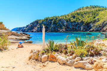 Wall Mural - Couple of unidentified people sunbathing on secluded Cala d'en Serra beach, Ibiza island, Spain