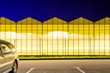 Parking near the luminous facade of the greenhouse. Greenhouse plant at night. Night landscape luminous glass construction.