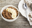 Chocolate oatmeal for breakfast with slices of a ripe banana and pieces of bitter good chocolate in a white ceramic bowl on a wooden background in a horizontal position. Example of a healthy die