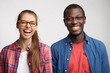 © WHstudio Leushin N - Interracial friends standing shoulder to shoulder having sincere smile and emotions. Young couple posing in studio with pleasant emotions. Caucasian woman with glasses and dark-skinned man smiling
