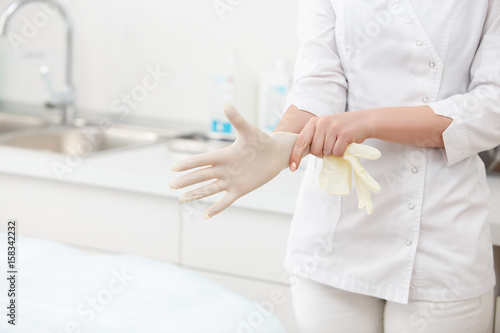 Fotografia, Obraz Blue latex medical gloves on a female hand, one hand pulls on a glove