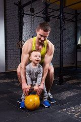 Happy father and little cute son exercising with dumbbells and smiling while against brick wall.