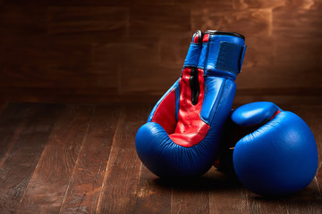 Two blue and red boxing gloves on brown wooden plank against wooden background.