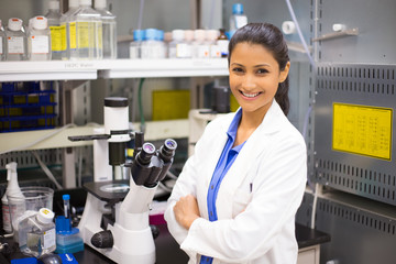 closeup portrait, young smiling scientist in white lab coat standing by microscope. isolated lab bac