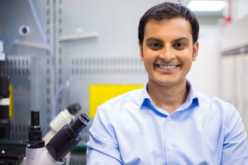 Closeup portrait, young friendly scientist standing by microscope. Isolated lab background. Research and development sector