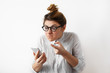 © shurkin_son - Portrait of a young indignant businesswoman with hair bun in glasses and shirt looking with anger at mobile phone. Disappointed confused female student. Negative human emotions, facial expressions