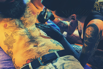 Wall Mural - Female tattoo artist makes tattoo on bearded male torso in a salon.