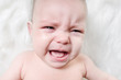 © R - Crying baby lies on a white fluffy background