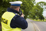 Fototapeta  - Kontrola radarowa przy drodze wojewódzkiej. Policjant dokonuje pomiaru prędkości w terenie zabudowanym.