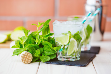 Two fresh mojitos cocktail in glass on wooden table. Mojitos with mint leaves, lime and ice. Drink making tools and ingredients for cocktail. 