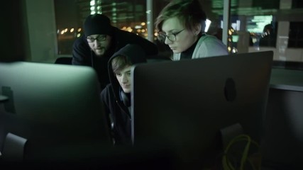 Wall Mural - tilt down of three cybercriminals working in team in front of computers in the dark office