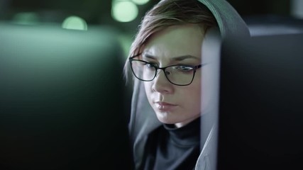 Wall Mural - closeup tracking shot of young woman in eyeglasses sitting in front of computer screen in the dark o