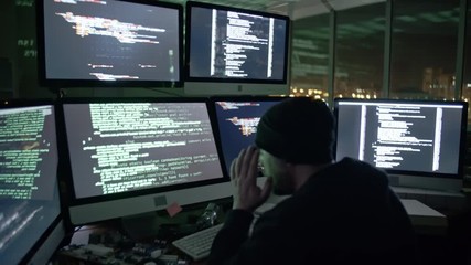 Wall Mural - tilt down of hacker working on six computer monitors in the dark office. man typing programming code