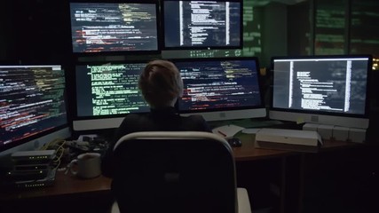 Wall Mural - rear view of female hacker sitting in the dark office in front of six monitors with data and typing 