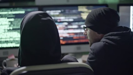 Wall Mural - tracking shot rear view of three hackers discussing how to crack network and typing on computers at 