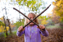 Young Girl In Woods Holding Two Sticks In A Cross Shape