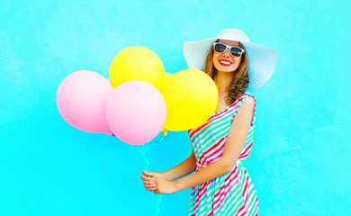 Summertime! Fashion smiling woman with an air colorful balloons is having fun on a blue background wearing a straw summer hat