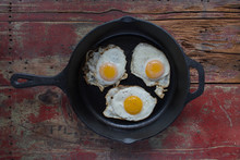 Three Sunny Side Up Fried Eggs In Cast Iron Pan On Wooden Table