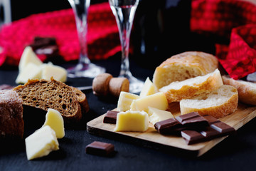 Alcoholic drinks, a holiday, white sparkling wine, glasses with champagne with freshly baked bread, mozzarella cheese and dark chocolate on a black wooden background 