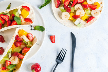 Summer snacks. Food for a party. Fruit tacos with strawberries, mangoes, bananas, chocolate, mint. On a light blue concrete table. Copy space top view