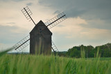 Old wooden wind mill with green field and cloudy sky