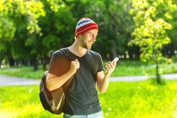 Young happy hipster man is standing at green summer park background and smiling.