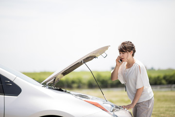 young woman checking under the hood and calling help with smart phone.