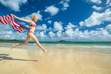 Patriotic Smiling Woman With American Flag Bikini Weaving American Flag. Female Jumping In Tropical Hawaiian Beach. Lanikai Beach In Oahu, Hawaii, USA. Freedom And Patriotic Concept. Indipendence Day.