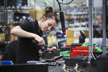 A Young Woman Using A Power Tool, A Skilled Factory Worker Assembling Cycle Parts.