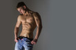 Sexy man with naked, strong torso stripping blue jeans