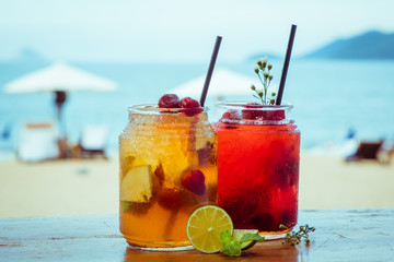 Close up of two glasses with refreshing strawberry cocktail with lime, apple and mint on sea beach background