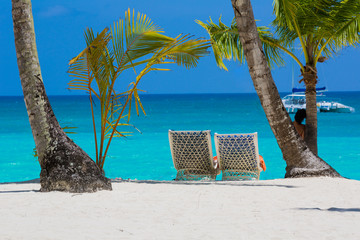 Sun beds for relaxing under coconut palms on a white bezke on a background of azure sea.