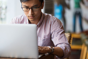 Concentrated young man typing on laptop in cafe